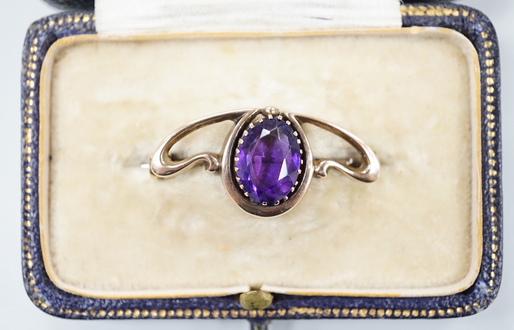 An Edwardian Art Nouveau 9ct and single stone oval cut amethyst set brooch, 31mm, gross weight 2.2 grams, in fitted gilt tooled leather box.